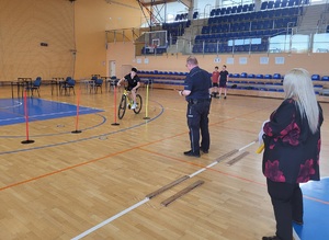 policjant stoi przy uczniu który na rowerze pokonuje tor  przeszkód