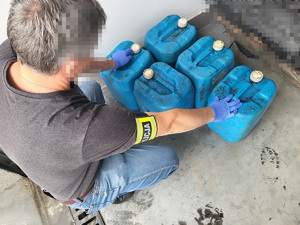 policjant w umundurowaniu cywilnym z opaską na rece z napisem policja trzyma bańki plastikowe, w których jest paliwo