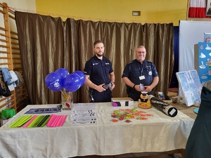 dwóch policjantówstoi przy stoliku, na którym lezą gadżety policyjne