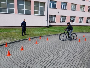 chłopiec jedzie na rowerze między pachołkami, czemu przygląda się policjant