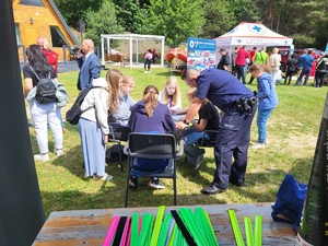 dzieci przy stoliku rozwiązuja krzyzówke, a policjant stoi obok i pomaga