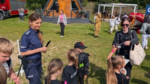 policjantka stoi przy dzieciach i trzyma w reku opaski odblaskowe