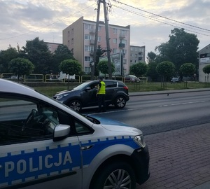policjant stoi przy samochodzie na drodze i podaje urządzenie do badania stanu trzexwości kierowcy