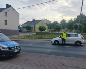 policjant stoi przy samochodzie na drodze i podaje urządzenie do badania stanu trzexwości kierowcy