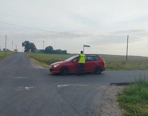 policjant stoi przy samochodzie na drodze i podaje urządzenie do badania stanu trzexwości kierowcy
