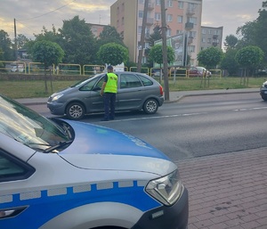 policjant stoi przy samochodzie na drodze i podaje urządzenie do badania stanu trzexwości kierowcy