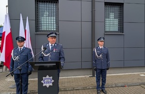 komendant powiatowy stoi na mównicy, po obu stronach stoją policjanci