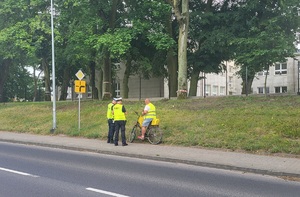 dwóch policjantów stoi przy rowerzyście na chodniku