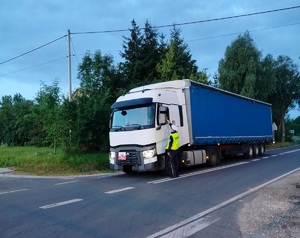 policjant stoi przy pojeżdzie zatrzymanym na drodze i sprawca stamn trzexowści