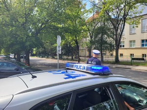 policjant stoi przy radiowozie przy szkole