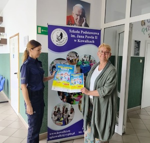 policjantka i jedna osoba stoja na tle baneru i trzymaja w ręku plakat