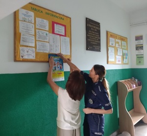 policjantka i jeszcze jedna osoba wieszaja plakat na tablicy ogłoszen