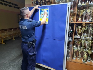 policjant wiesza na tablicy ogłoszen plakat