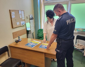 policjant i jeszcze jedna osoba stoja przy biuru na którym leża plakaty