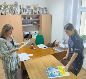 policjantka i jeszcze jedna osoba stoja  przy biurku i trzymaja w reku plakaty