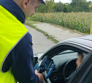 policjant przy samochodzie pokazuje wynik na rejestratorze prędkości