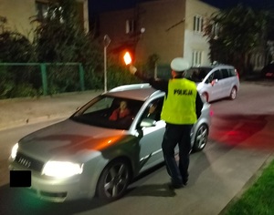 policjant stoi na drodze przy zatrzymanym pojezdzie