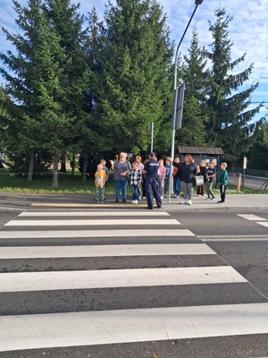 policjant stoi przed dziecmi przed przejsciem dla pieszych