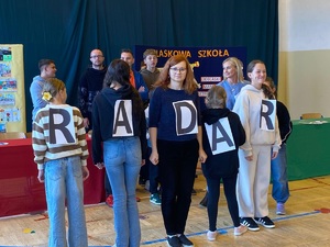 na scenie stoi pięć osób, która mają przyczepione do ubioru kartki z literami, które tworzą słowo &quot;radar&quot;