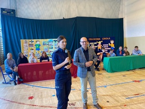 policjantka i jeszcze jedna osoba stoja na scenie przez zgromadzonymi osobami