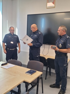 trzech policjantów, jeden z nich odczytuje list gratulacyjny