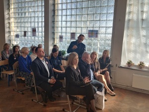 wiele osób siedzi na sali gimnastycznej, jeden policjant stoi  i wypowiada się do mikrofonu