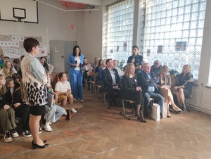 wiele osób siedzacych na sali, policjantka stoi i wypowiada się do mikrofonu