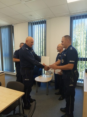 czterech policjantów, jeden z nich wrecza list gratulacyjny i podaje rekę