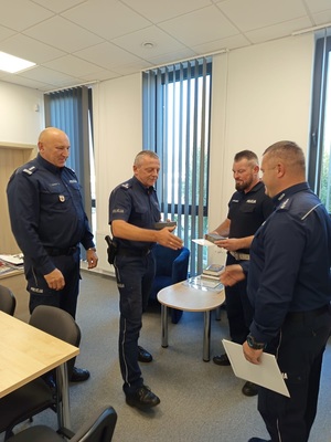 czterech policjantów, dwóch z nich podaje sobie rece