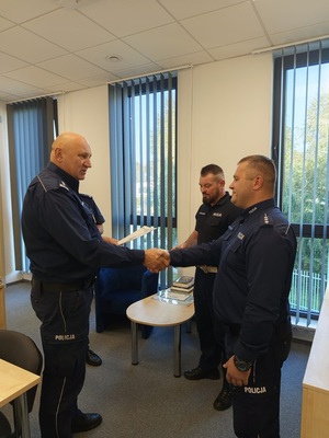 trzech policjantów, dwóch z nich podaje sobie rece
