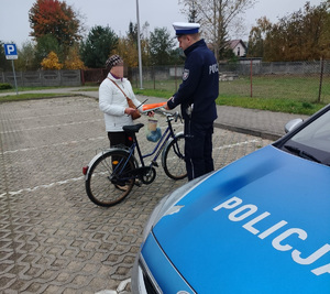 policjant wręcza opaski odblaskowe kobiecie, która stoi przy rowerze
