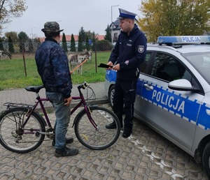 policjant wręcza opaske odblaskową mężczyżnie stojącemu przy rowerze
