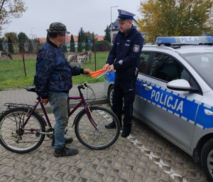 policjant wręcza opaske odblaskową mężczyżnie stojącemu przy rowerze