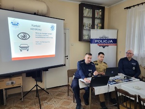 dwóch policjantów oraz strażak siedzą przy stole, w tle wyswietlana jest prezentacja
