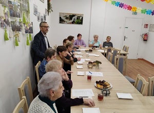 uczestnicy spotkania siedza przy stołach, jeden mężczyzna stoi