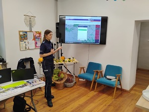 policjantka stoi przy ekranie telewizora i prowadzi prelekcje