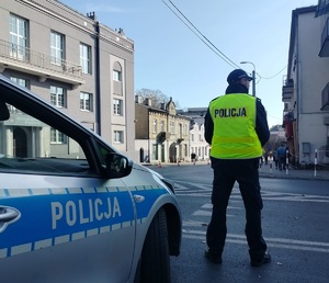policjant stoi przy radiowozie i obserwuje drogę