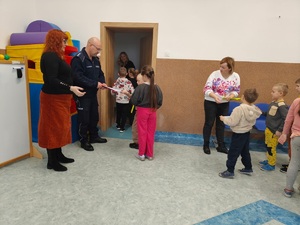 policjant stoi przy drzwiach i rozdaje dzieciom opaski, na zdjęciu około 10 osób