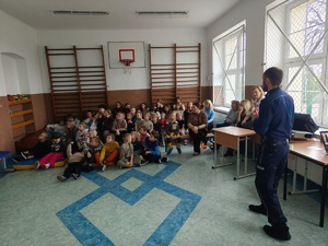 policjant stoi przed dziecmi i prowadzi prelekcję