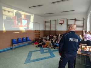 policjant stoi przed dziecmi i prezentuje film, na którym jest widoczy numer 112