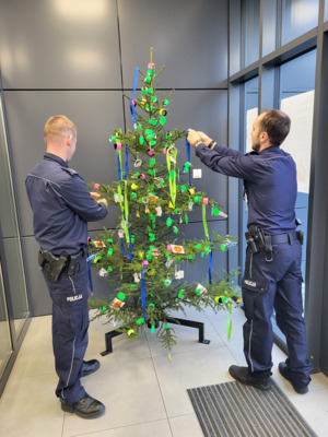 dwóch policjantów stoi przy choince i zawiesza ozdoby