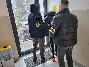 dwóch policjantów w umundurowaniu cywilnym prowadzi zatrzymanego