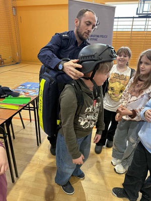 Policjant pomaga uczestnikowi założyć policyjny hełm