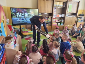 policjant przy pomocy tuby pokazuje dzieciom jak wygladają odblaski