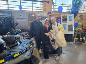 zdjecie policjanta i uczestników wydarzenia na tle policyjnegostanowiska