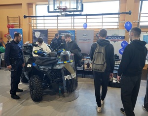 uczestnicy wydarzenia stojący przy policyjnym stanowisku, jeden z nich wsiada na quada