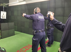 policjant oddaje strzał do tarczy, a za nim stoi prowadzacy stzrelanie