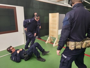 policjant po przeniesienie rannego policjanta za osłonę wydobywa broń by oddać strzały do tarczy