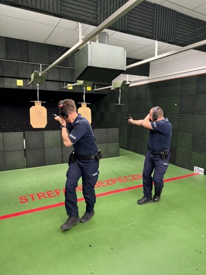 dwóch policjantów oddaje strzały do tarczy, jednaczesnie osłaniając twarz