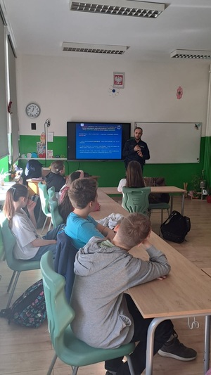 policjant stojący przed dziećmi w klasie, dzieci siedzą w ławkach